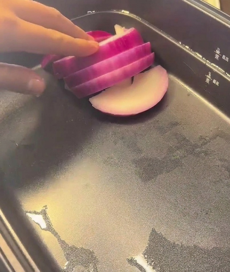 Une main déposant de belles tranches doignon rouge au fond dune marmite électrique noire.