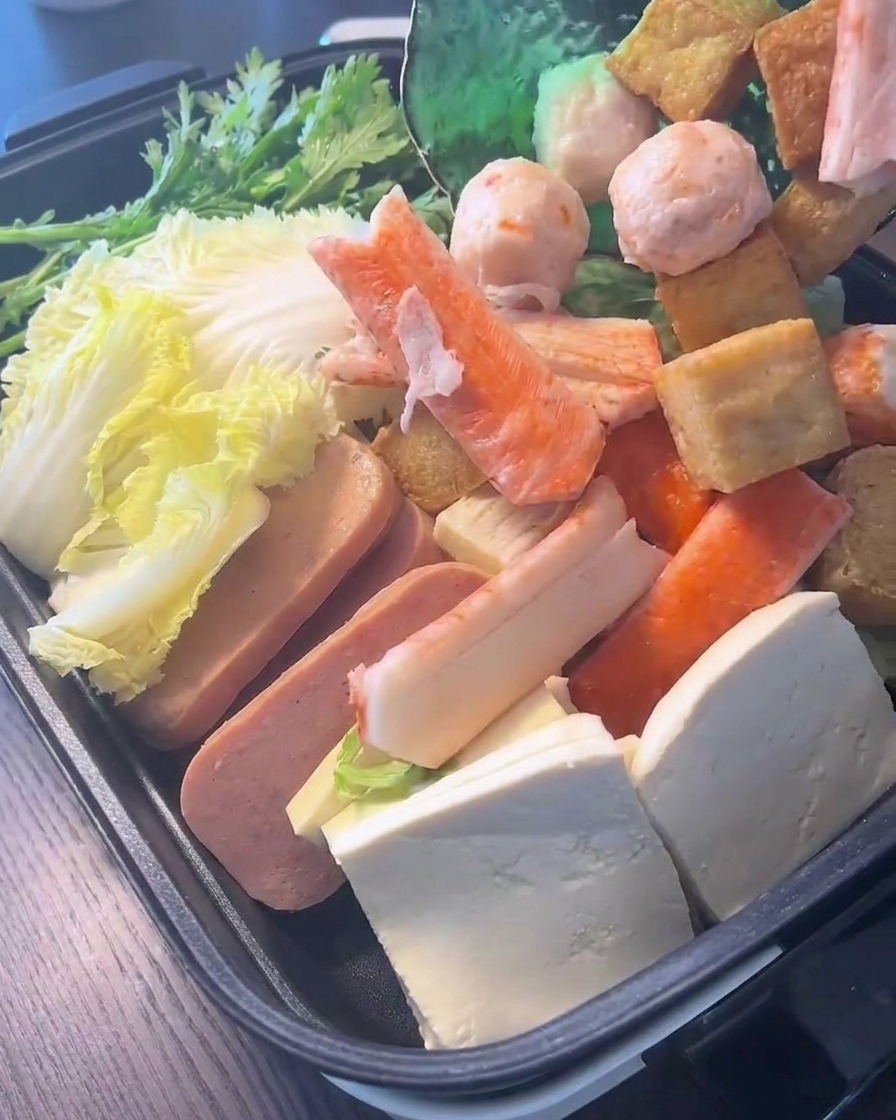 Un assortiment de boulettes de poisson et de bâtonnets de crabe déposés sur des feuilles de chou fraîches dans la marmite de cuisson.