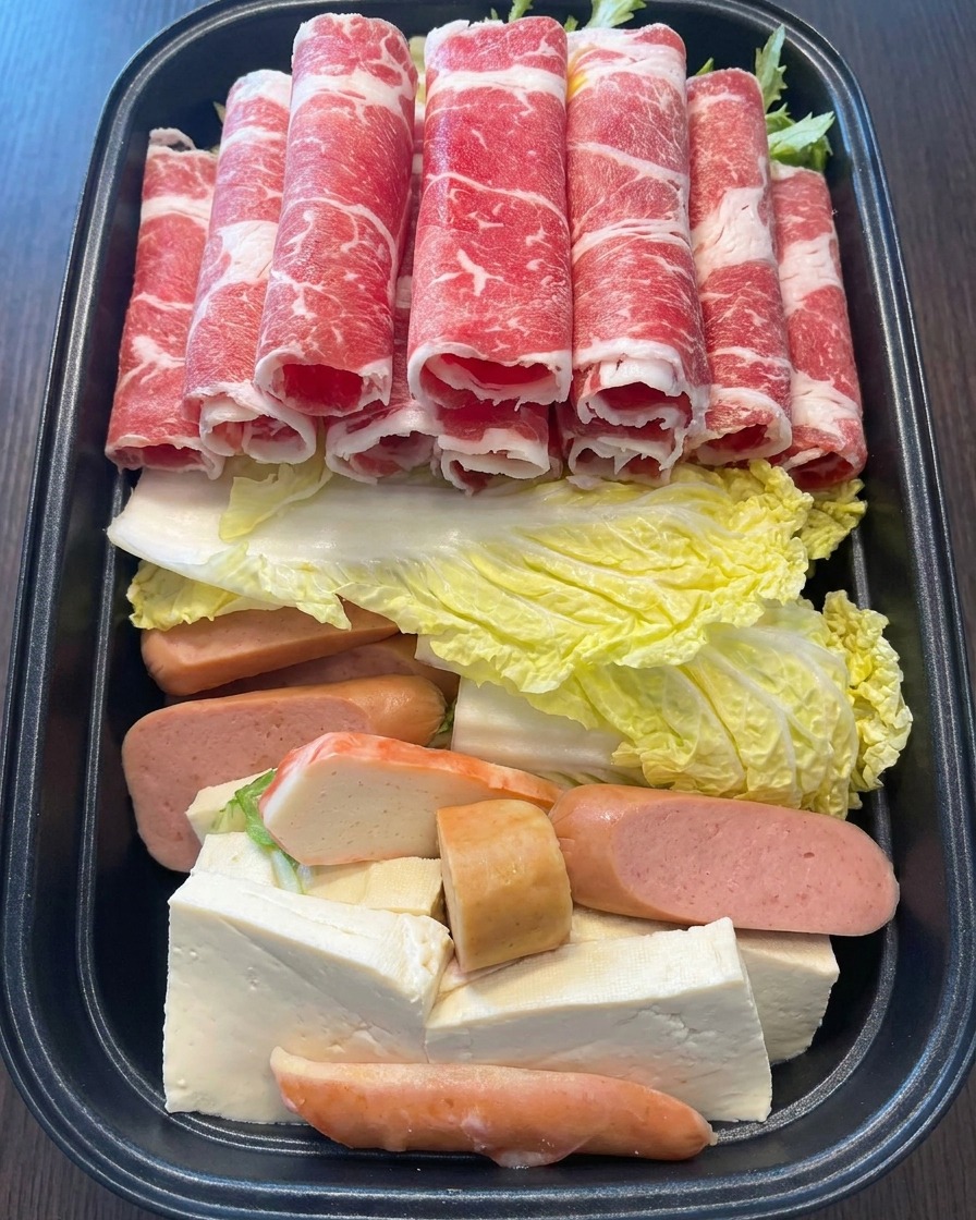 Une main déposant délicatement plusieurs fins rouleaux de bœuf persillé dun rouge éclatant sur lassemblage coloré de la marmite.