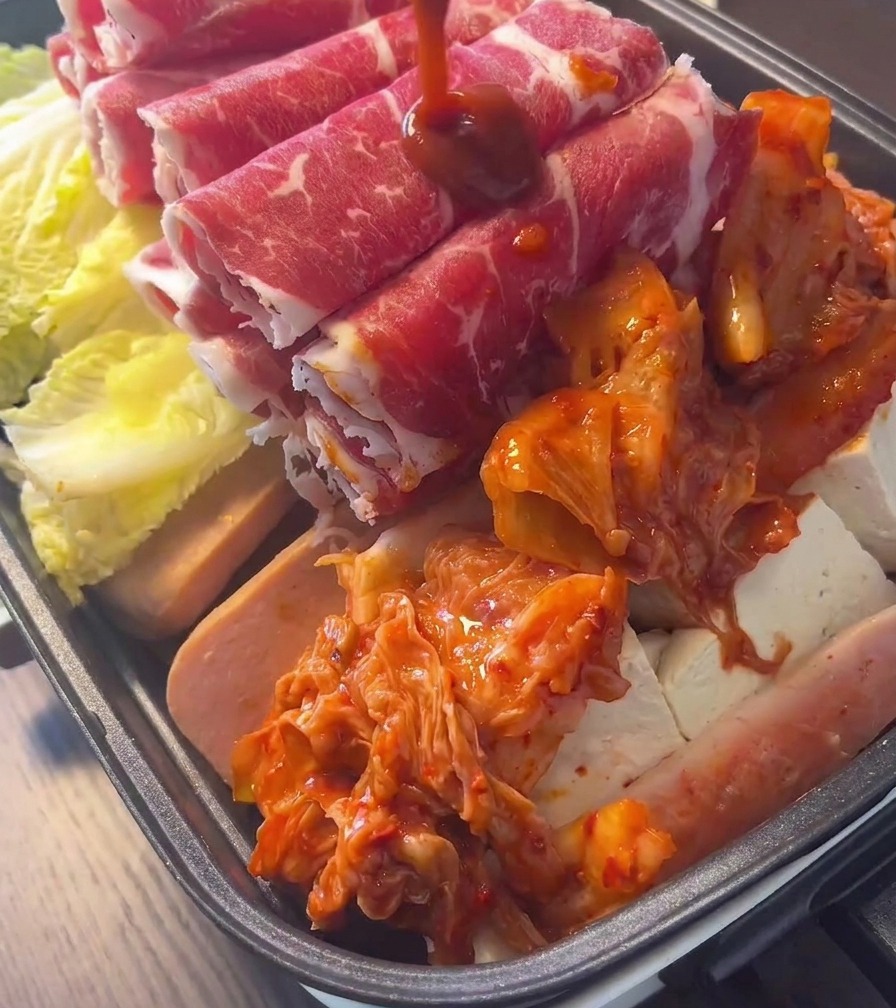 Un généreux dôme de kimchi fermenté dun rouge intense, déposé au centre dune marmite remplie de viande et de légumes.