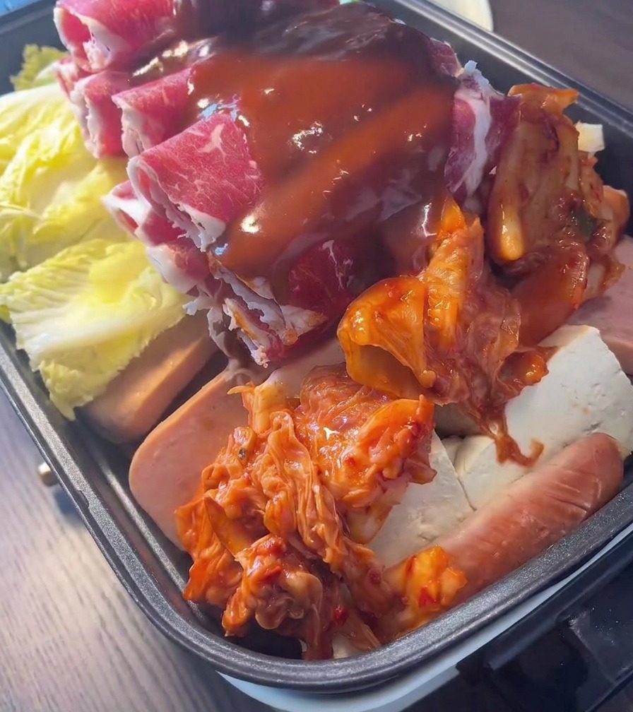 Une sauce piquante coréenne rouge et onctueuse versée en filet sur une marmite garnie de bœuf, de kimchi et de légumes.