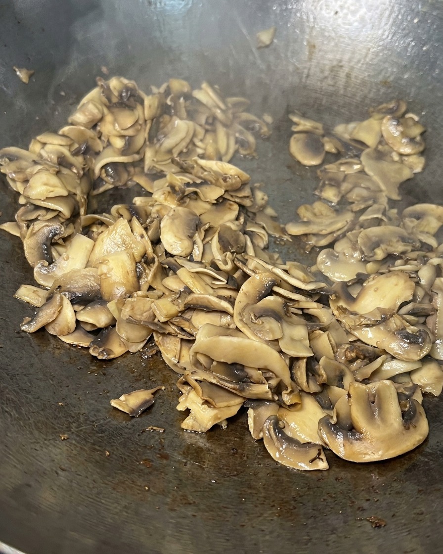 Tranches de champignons sautées dans une poêle, désormais réduites, bien dorées et presque sèches.