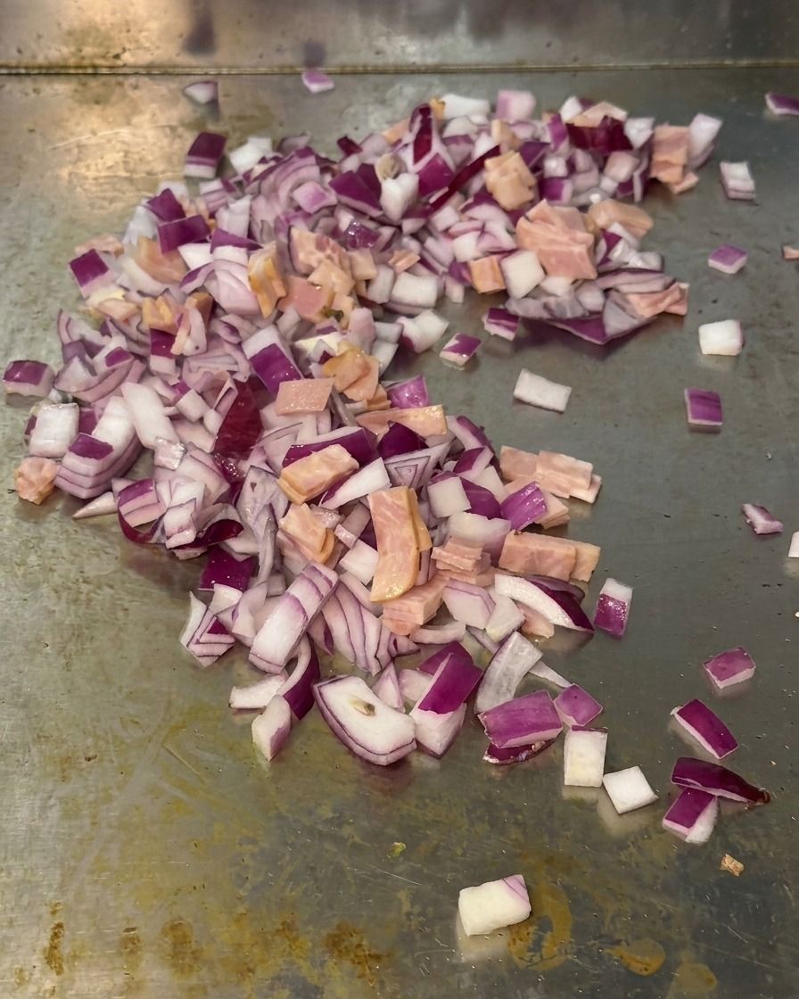 Mélange doignons rouges en dés et de petits morceaux de lardons sautés ensemble sur la surface dun gril métallique.