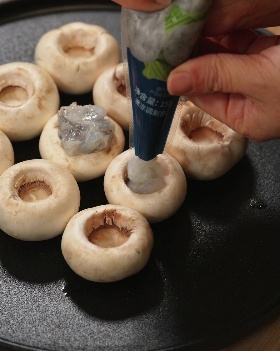 Une main garnissant de pâte de crevettes crue la cavité dun chapeau de champignon frais.