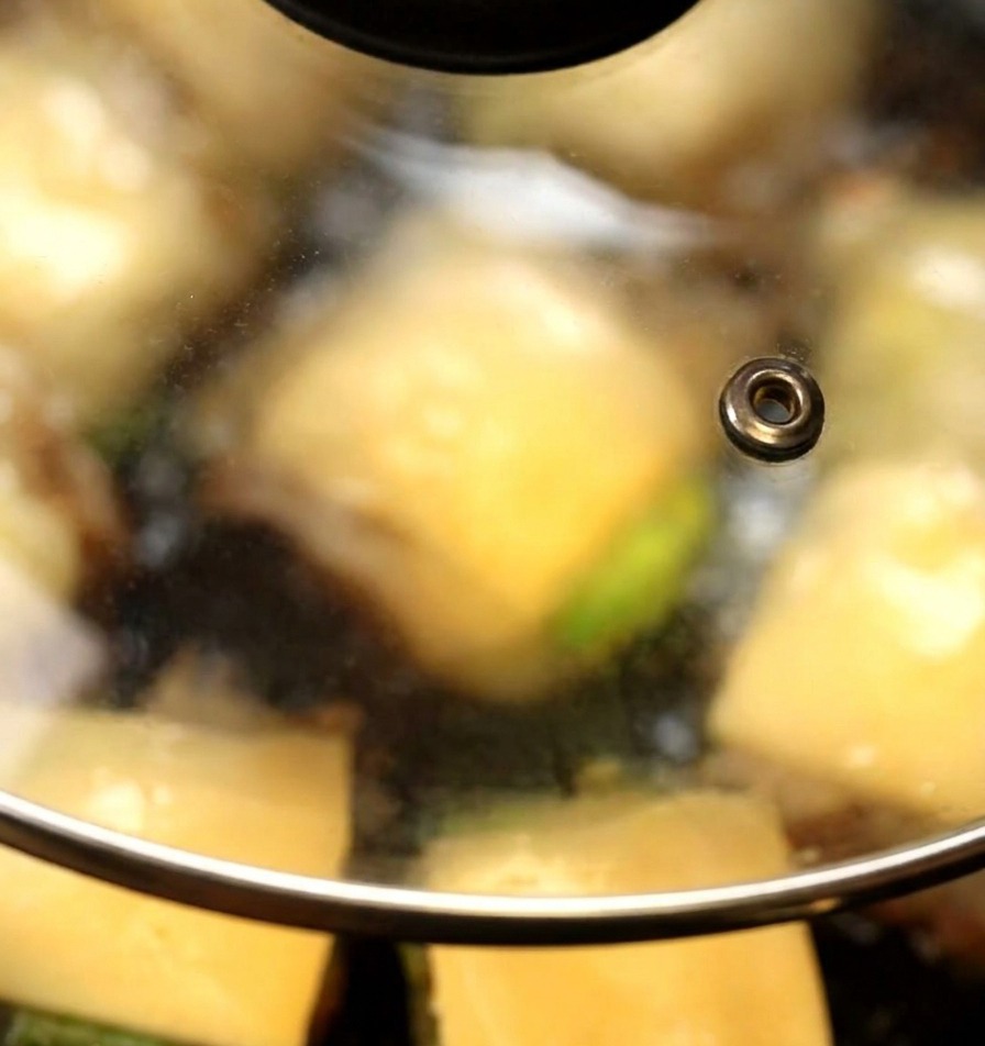 Un couvercle en verre recouvrant une poêle où des tranches de fromage commencent à fondre sur des burgers de champignons.