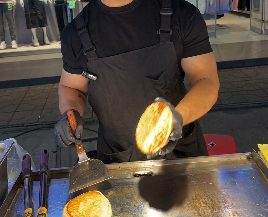 Une personne tenant une moitié de pain à burger parfaitement dorée au-dessus dune plaque de cuisson en acier inoxydable.