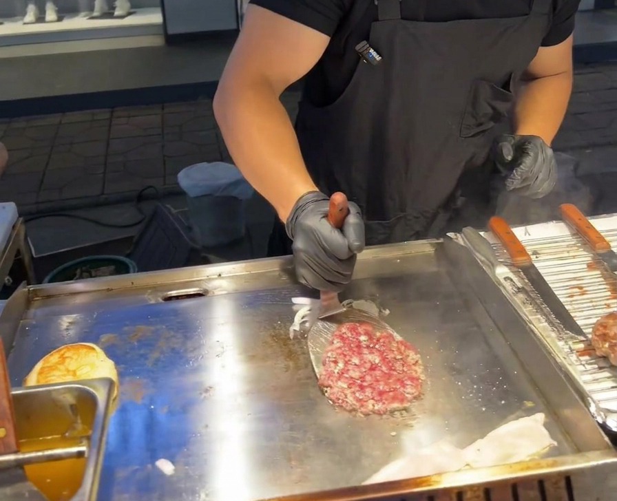 Une spatule en métal retournant un steak de bœuf sur un tas doignons rouges grillés.