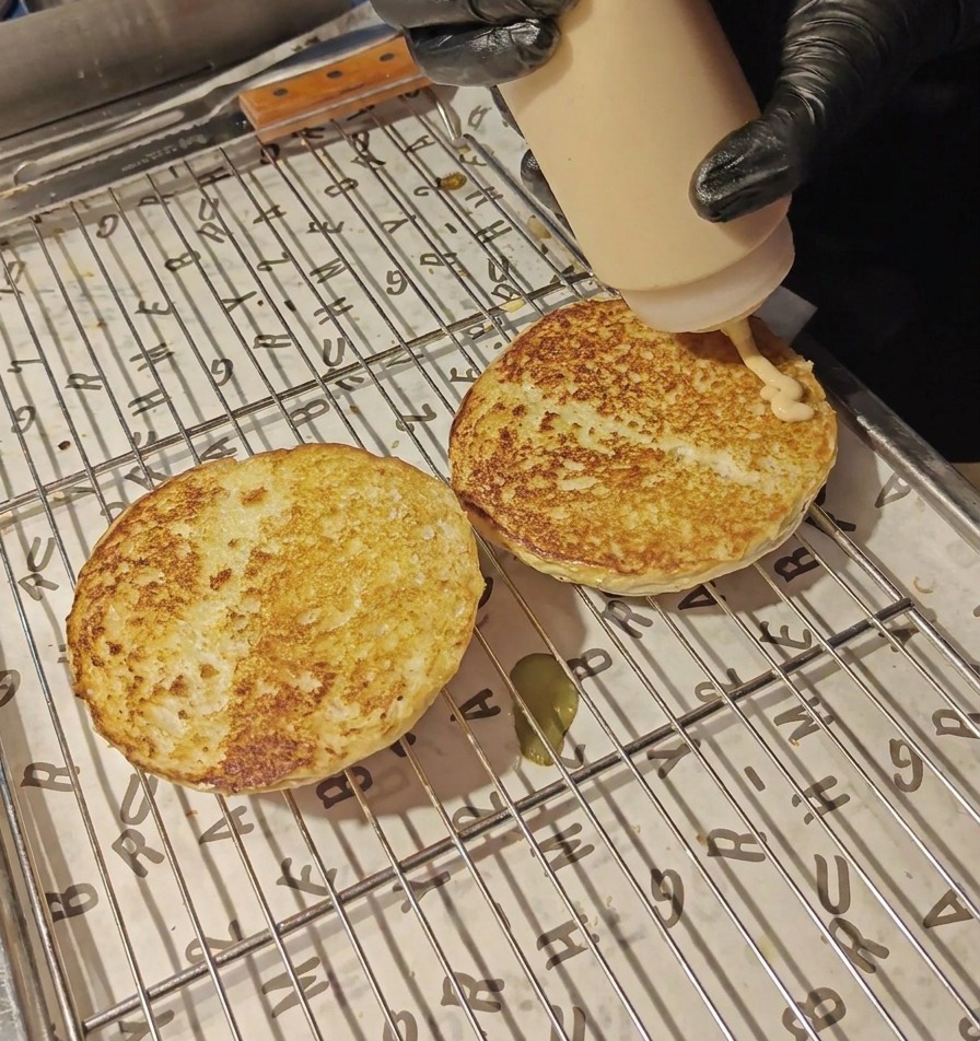 Une sauce crémeuse orangée versée depuis un flacon souple sur les deux moitiés de pain toastées.