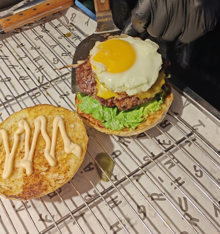 Une spatule en métal transférant le steak recouvert de fromage fondu et dun œuf au plat sur le lit de laitue et de tomate.