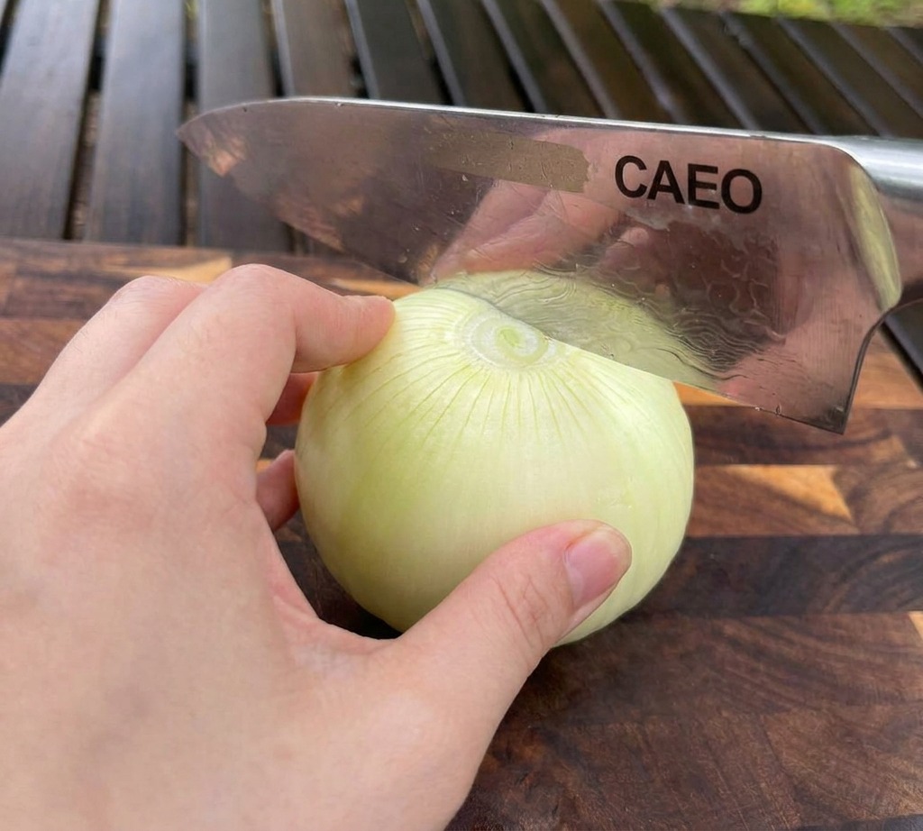 Une main maintenant un oignon blanc sur une planche à découper en bois tandis quun couteau de chef le tranche finement.