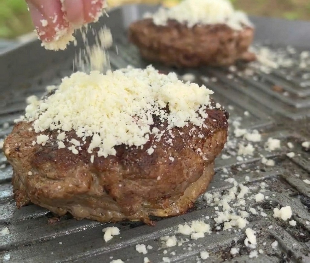 Gros plan sur du fromage blanc râpé saupoudré sur un steak de bœuf doré dans une poêle-gril bien chaude.