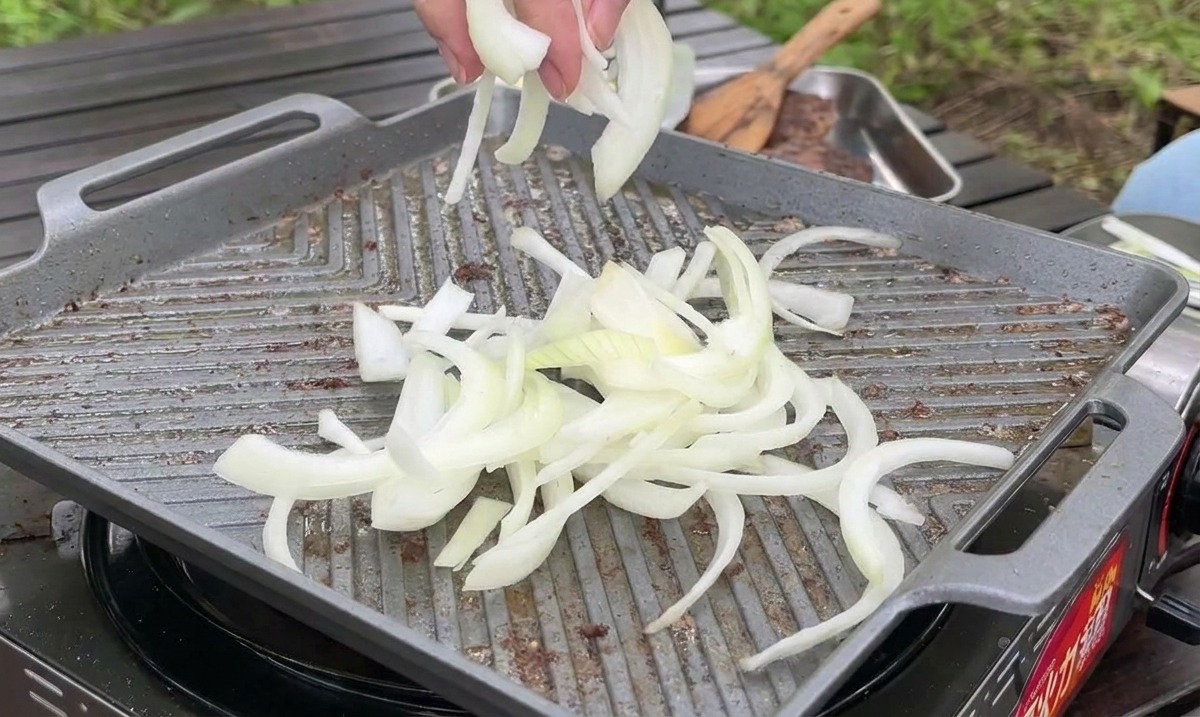 De fines tranches doignons blancs jetées sur une plancha très chaude pour être sautées à côté de la viande.