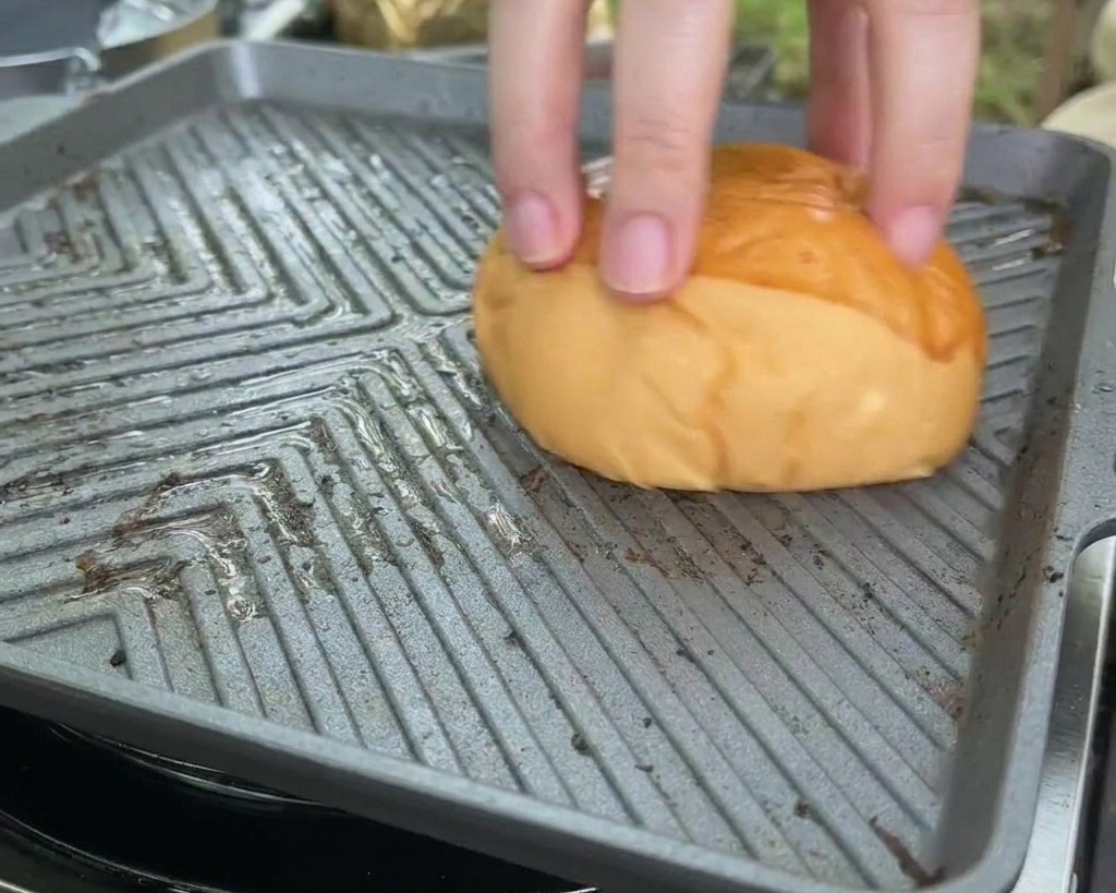 Un pain brioché pressé face vers le bas sur une plancha carrée chaude pour griller la mie.