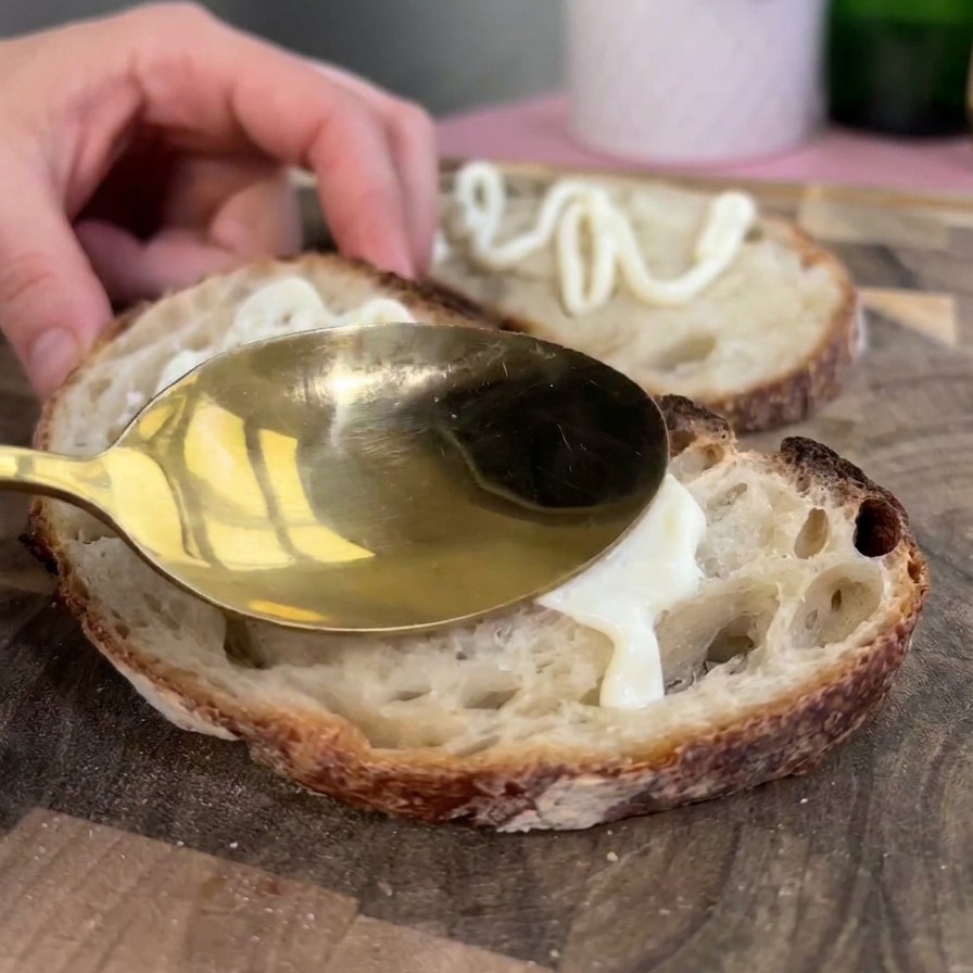 Une cuillère dorée étalant une couche épaisse de mayonnaise blanche sur une tranche de pain au levain rustique toastée.