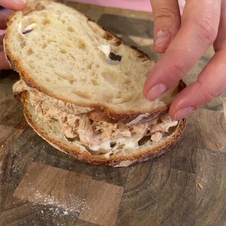 Des mains posant une tranche de pain au levain toastée sur un dôme de poulet effiloché pour refermer le sandwich.