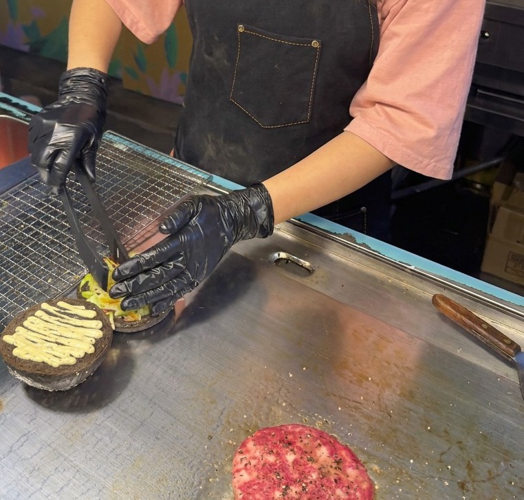 Une pince de cuisine déposant un mélange de laitue et de chou rouge émincés sur un pain noir déjà nappé de sauce à la truffe.