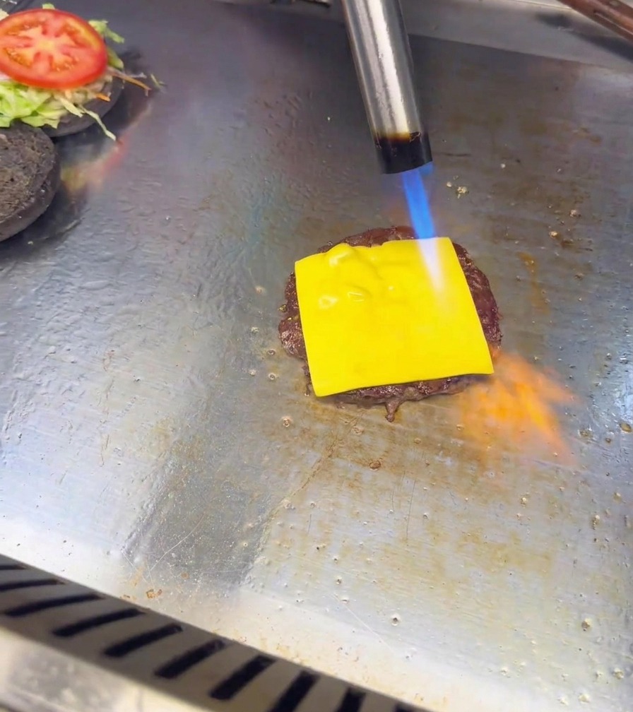 La flamme bleue et orange dun chalumeau de cuisine faisant fondre une tranche de fromage sur un steak de burger.