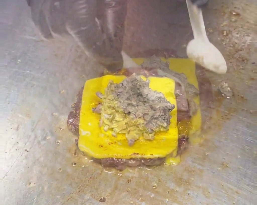 Une cuillère étalant une sauce épaisse et crémeuse aux champignons gris-brun sur un steak de cheeseburger.