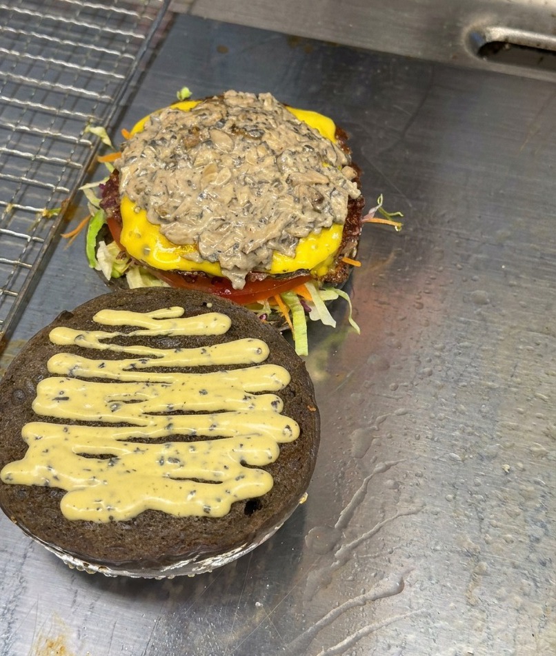 Une pile de champignons sautés émincés reposant sur un steak de burger monté avec du fromage et de la sauce.