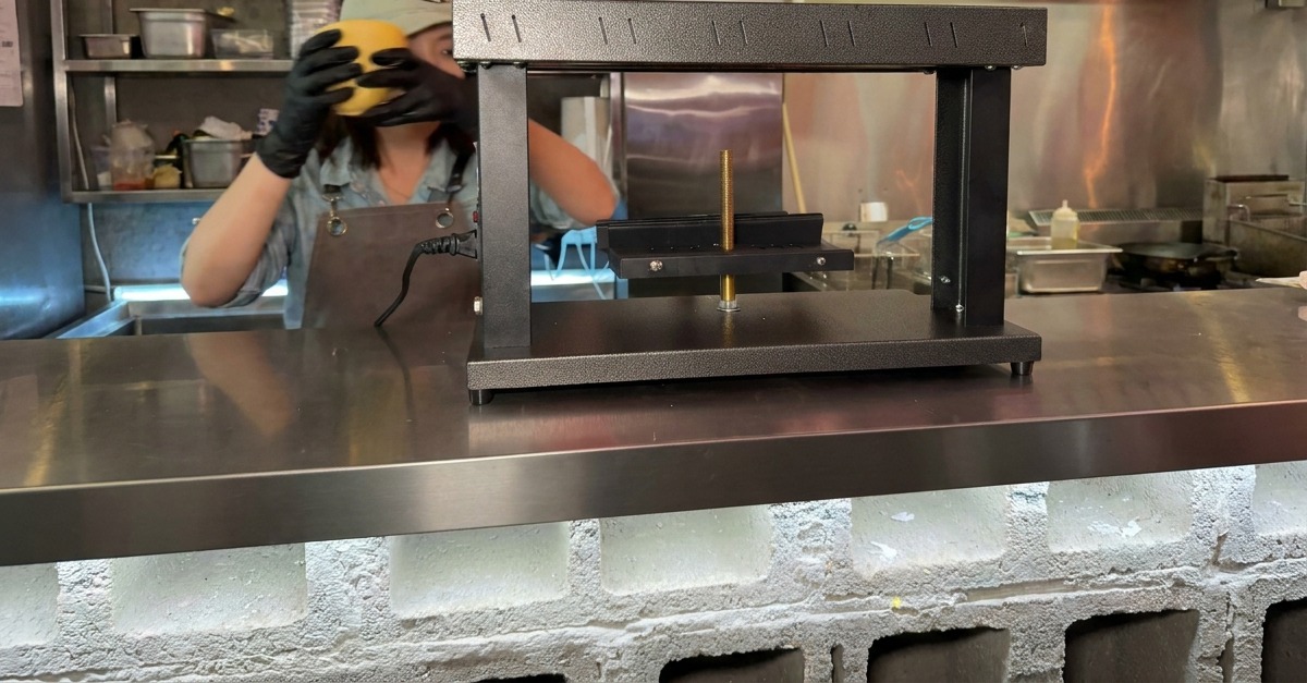 Mains plaçant un bloc de fromage en demi-meule sur le support dun appareil à raclette professionnel.