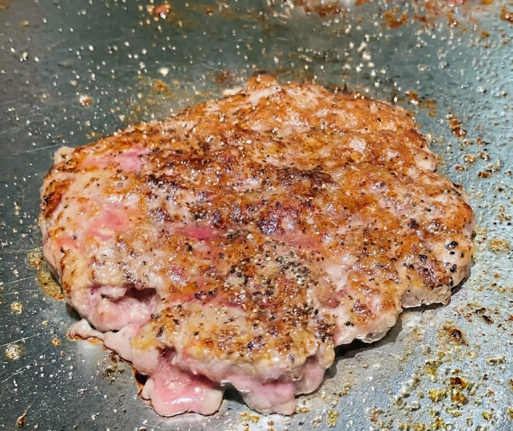 Un steak de bœuf retourné sur un gril révélant une surface croustillante profondément saisie et dorée.