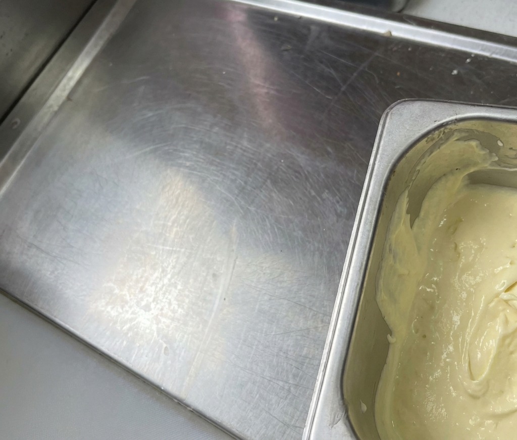 Un récipient en métal rempli dune sauce onctueuse jaune clair à laspect lisse et crémeux.