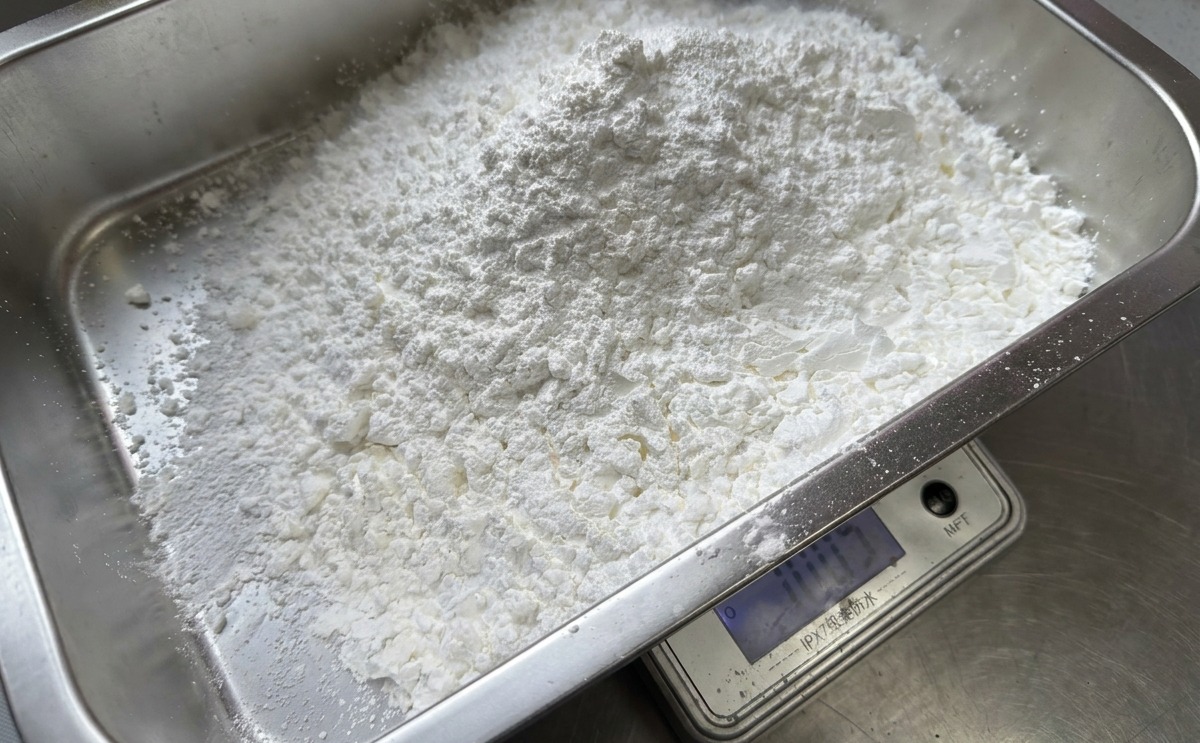Une grande quantité de fécule de maïs blanche pesée sur une balance digitale dans un bac rectangulaire en acier inoxydable.