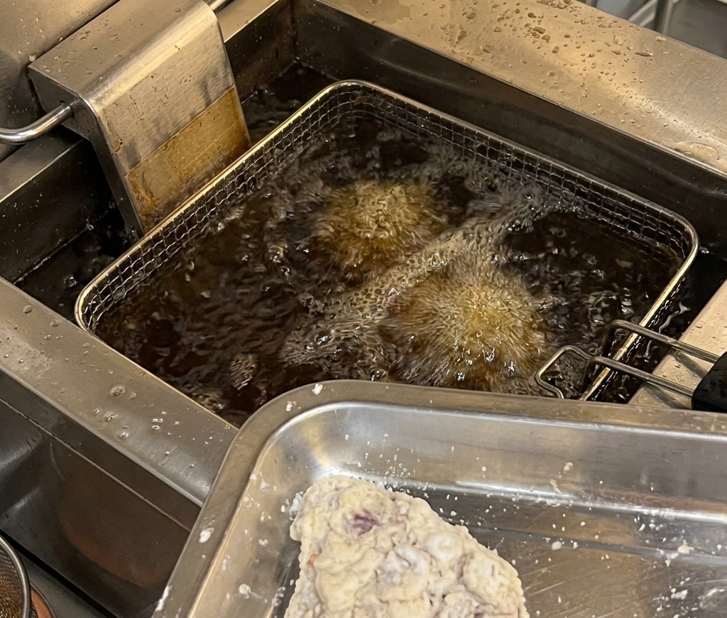 Des morceaux de poulet panés sur un plateau en métal prêts à être plongés dans une friteuse professionnelle à lhuile chaude et bouillonnante.