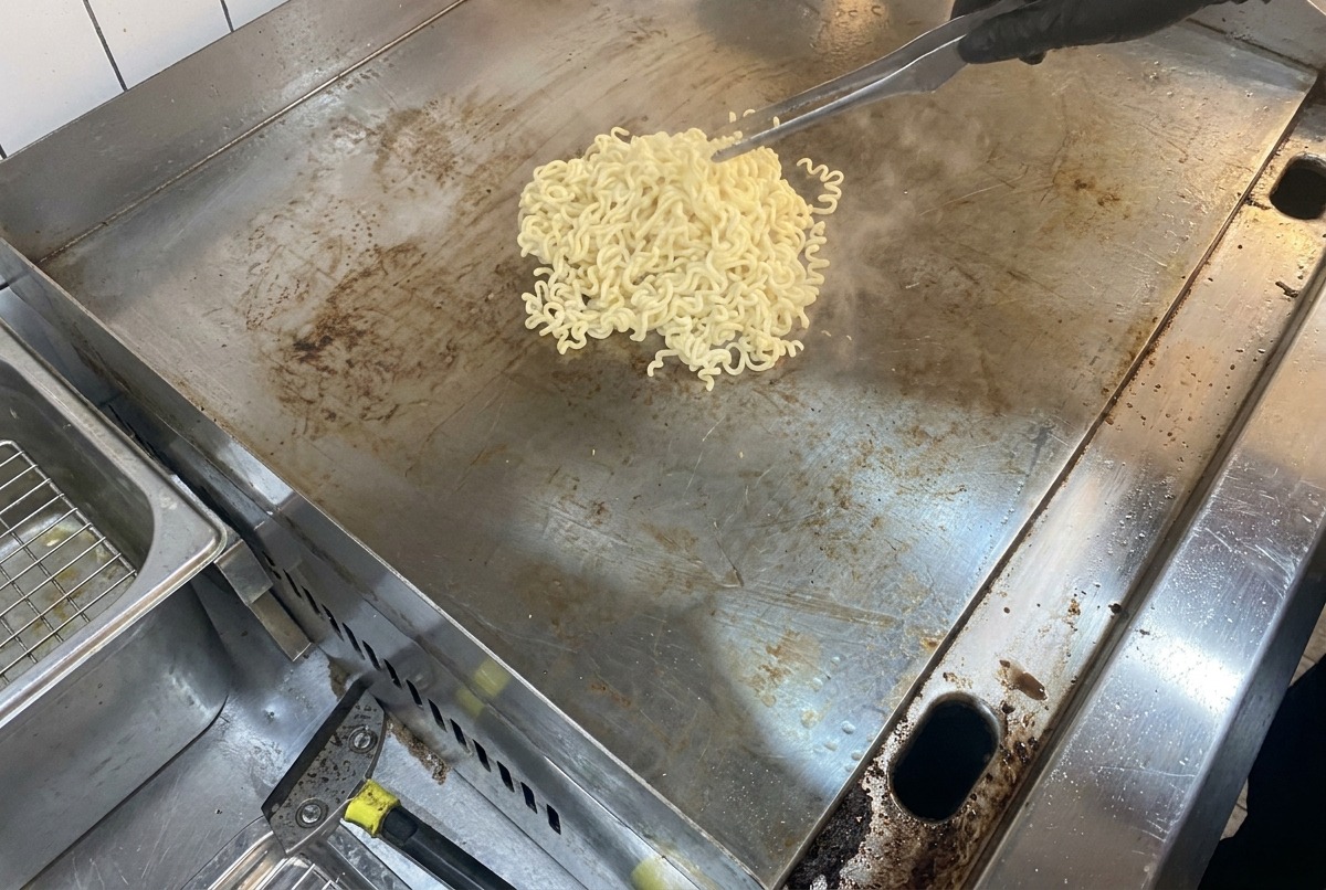 Des nouilles fumantes et du beurre en train de fondre sur une grande surface de cuisson en métal plate.