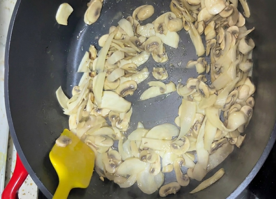 Des champignons émincés remués dans une poêle de cuisson sombre à laide dune spatule jaune vif.