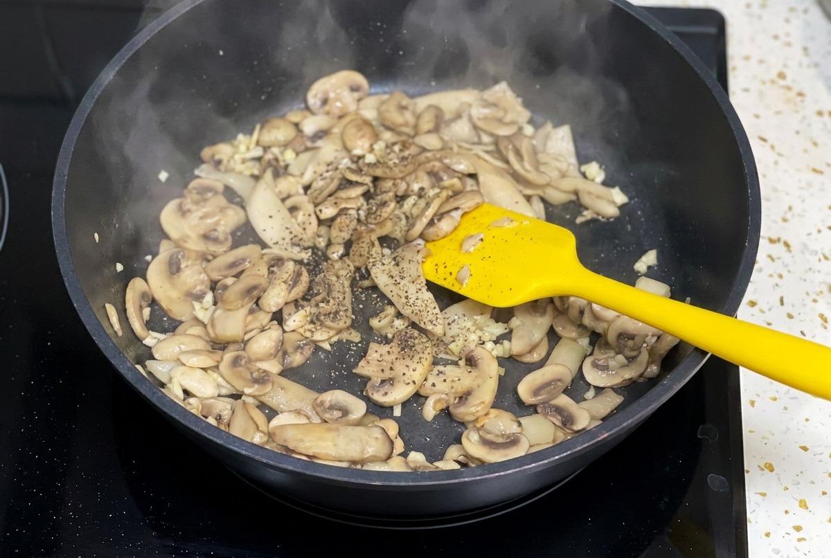 Des champignons sautés dans une poêle noire sur lesquels on saupoudre du poivre noir moulu.