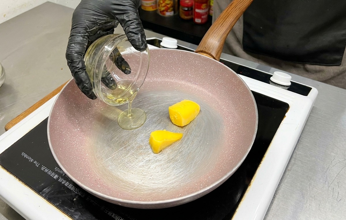 Deux morceaux de beurre jaune dans une poêle alors que de lhuile dolive est versée depuis un bol en verre.