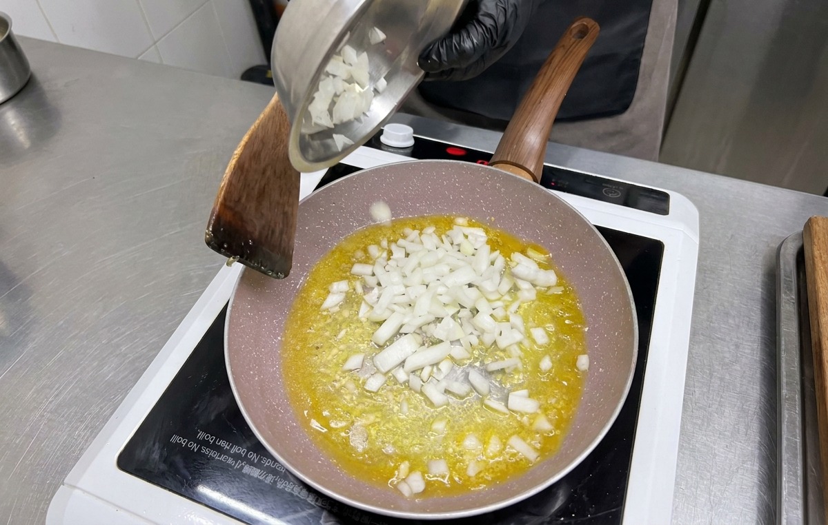 Des oignons blancs coupés en dés versés depuis un bol en métal dans la poêle contenant lail et le beurre.