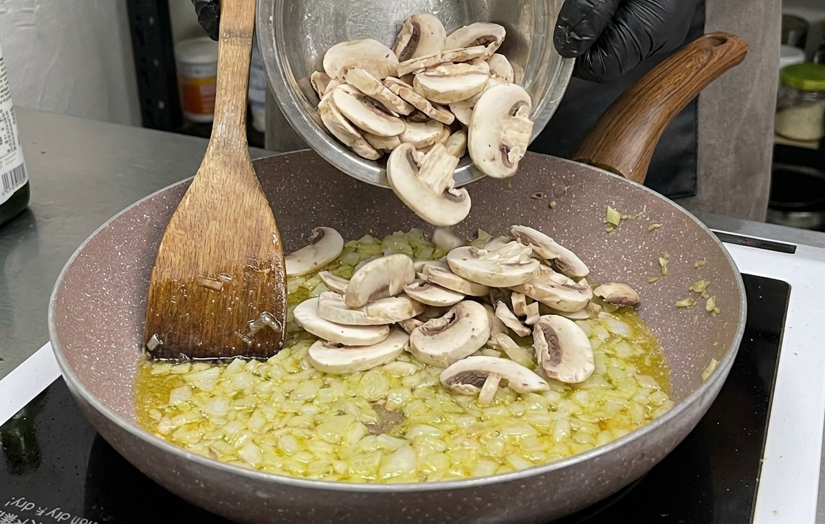 Un grand bol de champignons de Paris crus et émincés ajoutés à la poêle doignons et dail revenus.