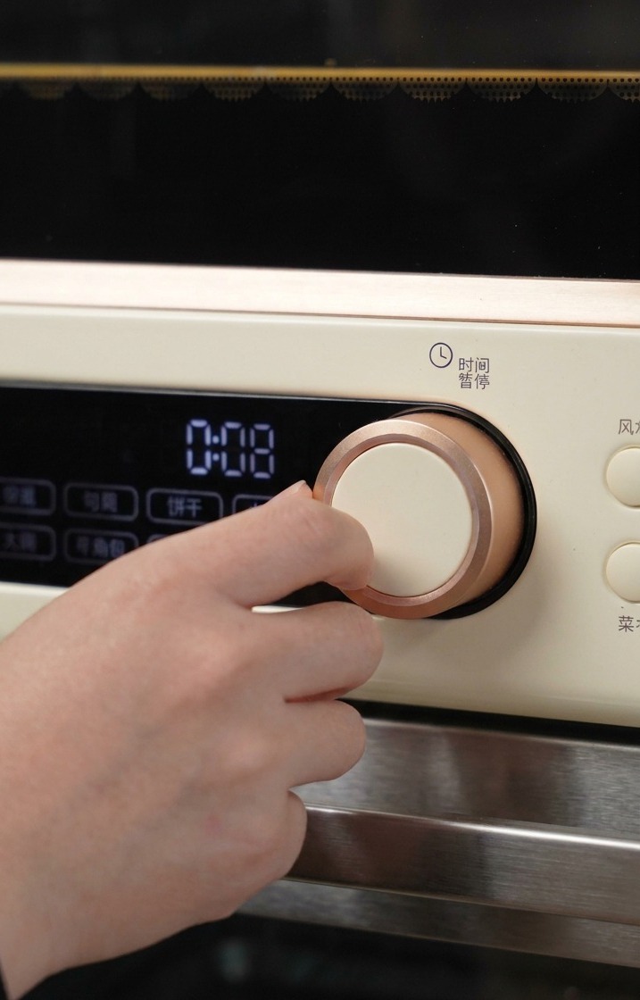 Une main tournant le bouton en or rose dun four de couleur crème pour régler le temps et la température de cuisson initiaux.