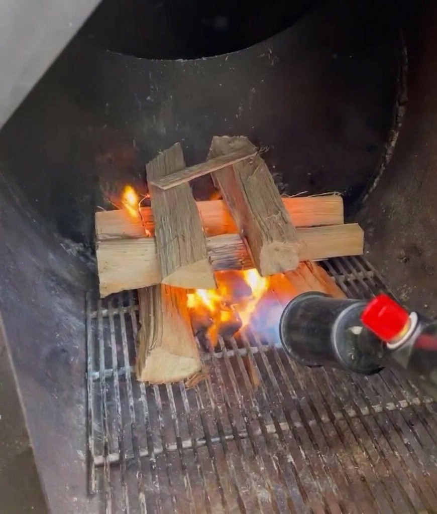 Un chalumeau au propane utilisé pour embraser une pile de bûches de chêne fendu à lintérieur du foyer en métal dun fumoir.