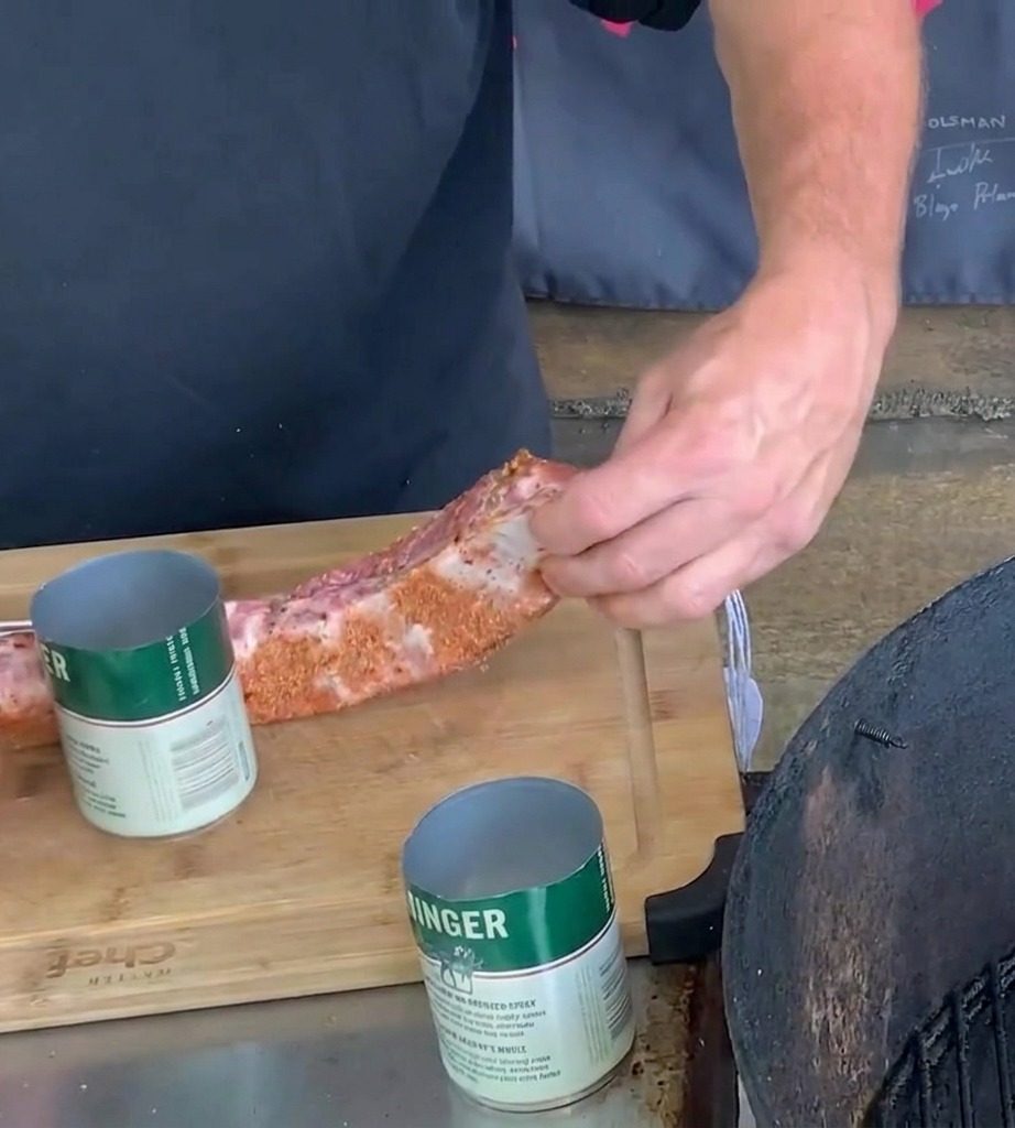 Une paire de mains enroulant une bande de porc épicée autour dune canette de bière en métal verte et blanche sur une planche en bois.