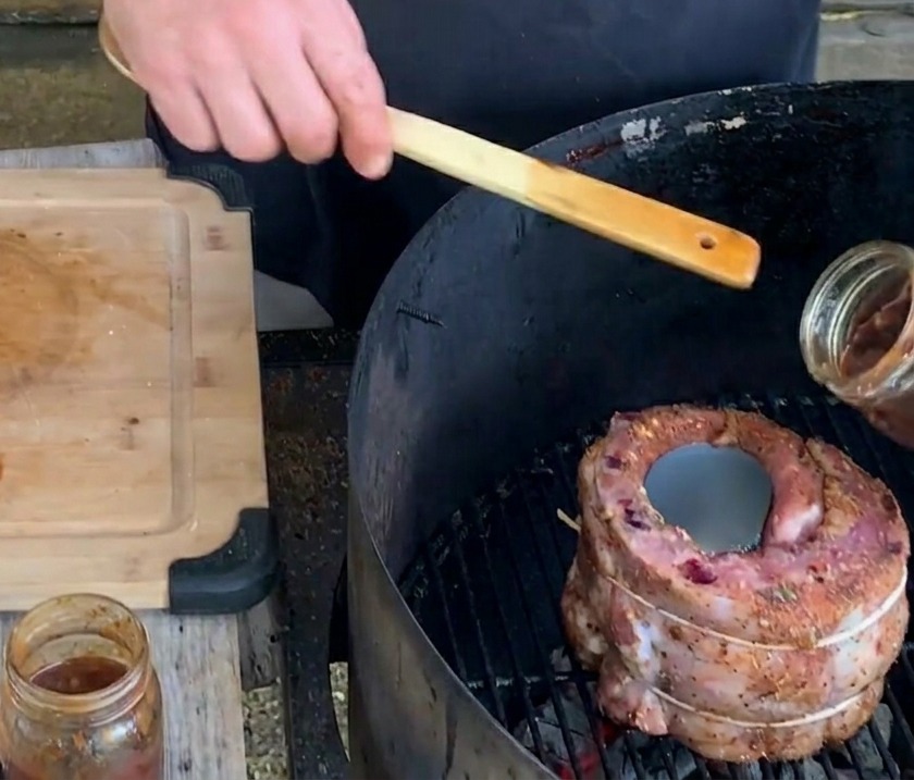 Une main verse une sauce aux bleuets épaisse et foncée depuis un bocal en verre dans une canette en métal au centre dune coupe de viande sur le gril.
