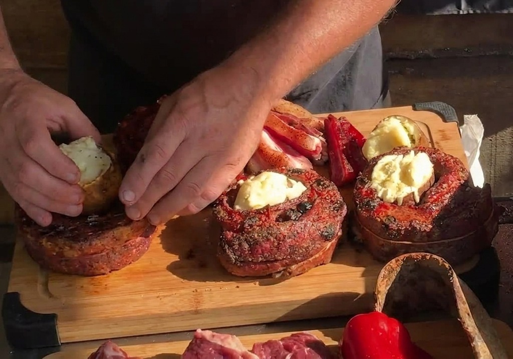 Des mains insérant délicatement une pomme de terre entière rôtie au centre creux dune bande de porc cuite et circulaire sur une planche en bois.