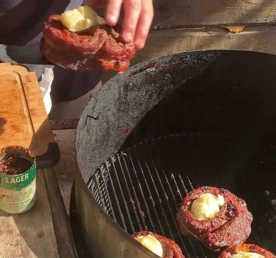 Une personne plaçant une coupe de viande farcie sur la grille du barbecue, à côté dautres coupes et de tranches de bacon.