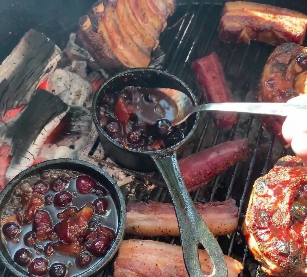 Une personne utilisant une cuillère pour napper de sauce aux bleuets foncée des coupes de porc grillées et farcies de pommes de terre depuis une petite marmite en fonte.