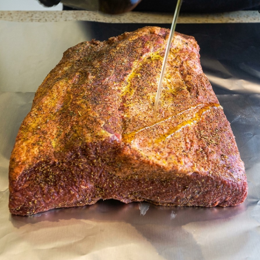 Un fin filet dhuile dolive versé sur le brisket de bœuf enrobé dépices et posé sur du papier aluminium.