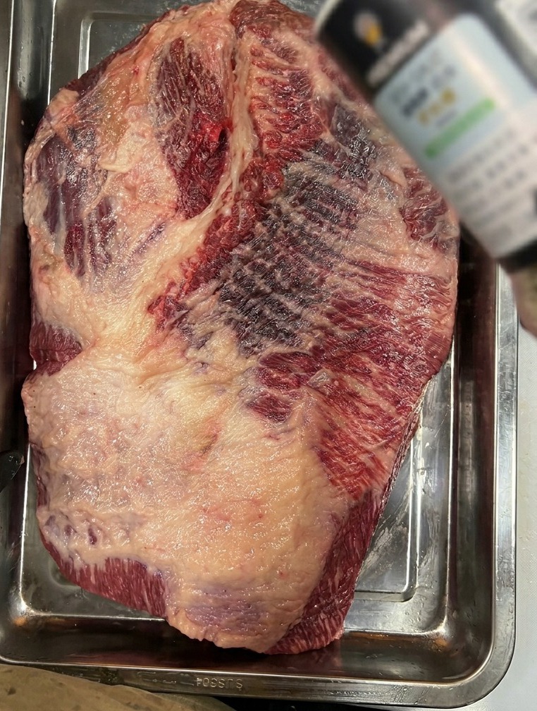 Gros sel de mer saupoudré sur une grande poitrine de bœuf brute déposée dans un plat en acier inoxydable.