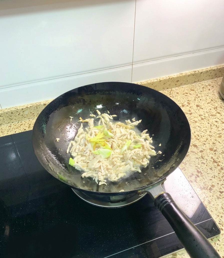 Effiloché de poulet partiellement cuit et opaque dans un wok, mélangé avec des morceaux doignons verts frais et des tranches de gingembre.