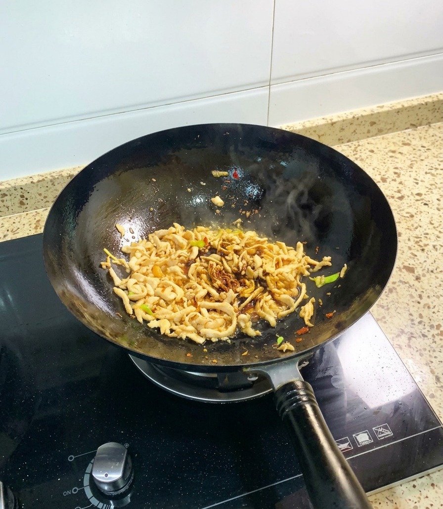 Poulet effiloché dans un wok noir, sauté avec de la sauce soja foncée et une dose visible de sauce dhuître épaisse.