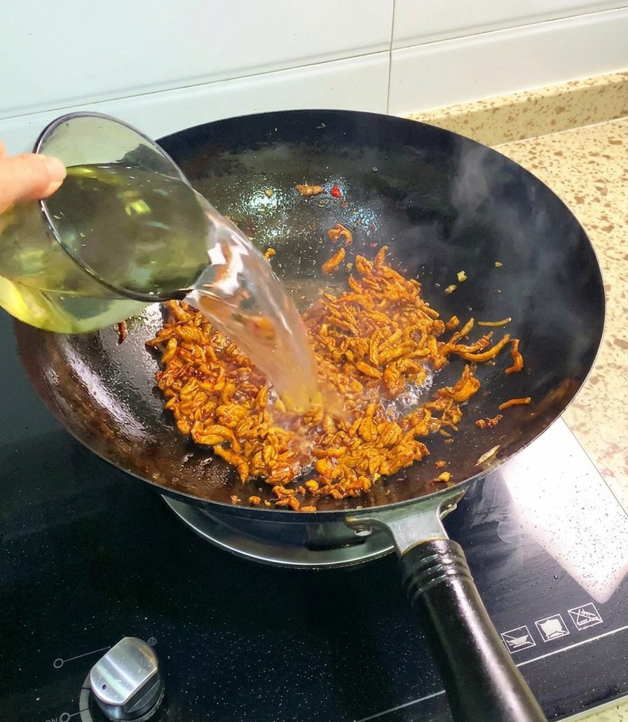 Un filet deau claire versé depuis un verre dans un wok rempli deffiloché de poulet sauté et assaisonné.