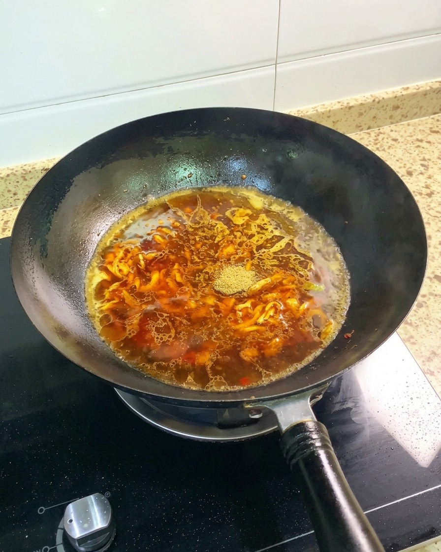 De la poudre de cinq-épices et un anis étoilé entier posés à la surface du bouillon brun-rouge dans un wok noir.