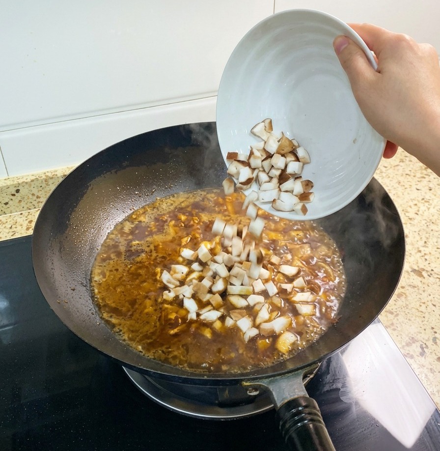 Une poignée de champignons shiitake coupés en dés ajoutée au bouillon brun-rouge qui mijote dans un wok.