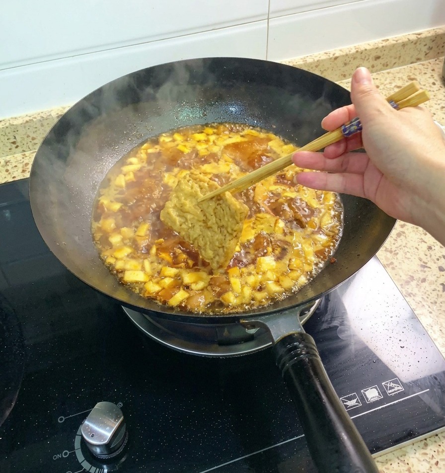 Une tranche de tofu frit tenue par des baguettes et plongée dans la sauce bouillonnante aux champignons et au poulet.
