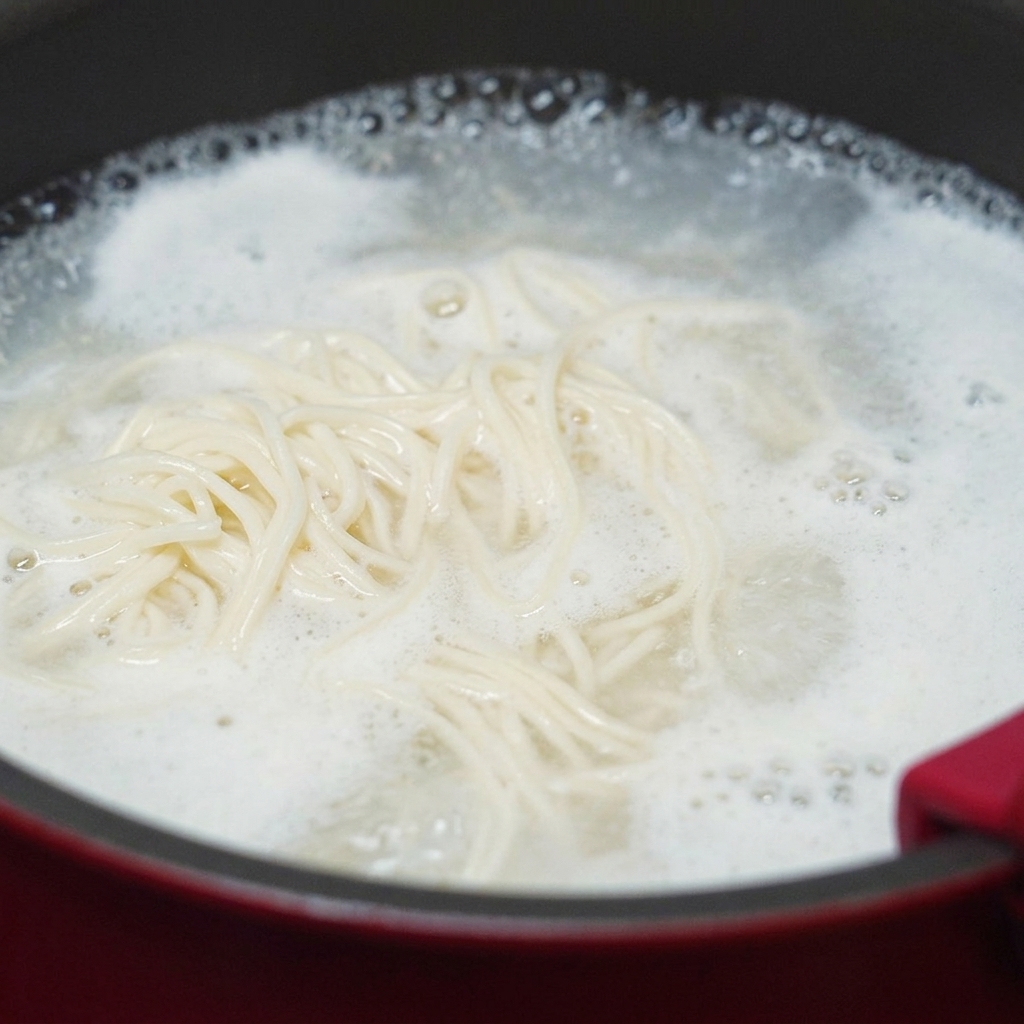 Des nouilles de blé blanc tourbillonnant dans une casserole deau bouillante avec une épaisse mousse damidon sur les bords.